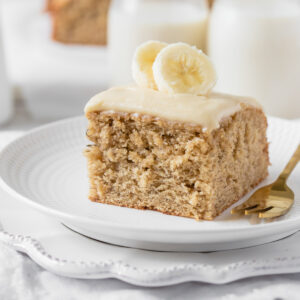 A square slice of the banana cake garnished with fresh banana slices.