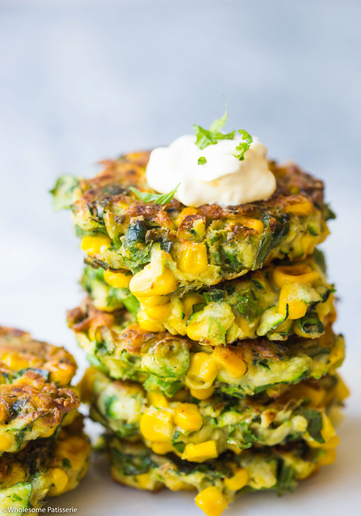 A stack of the fritters with a dollop of sour cream and fresh parsley on top.