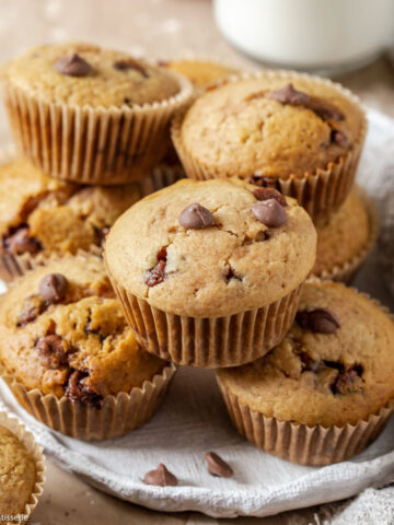 Muffins stacked together on a plate with chocolate chips scattered around.