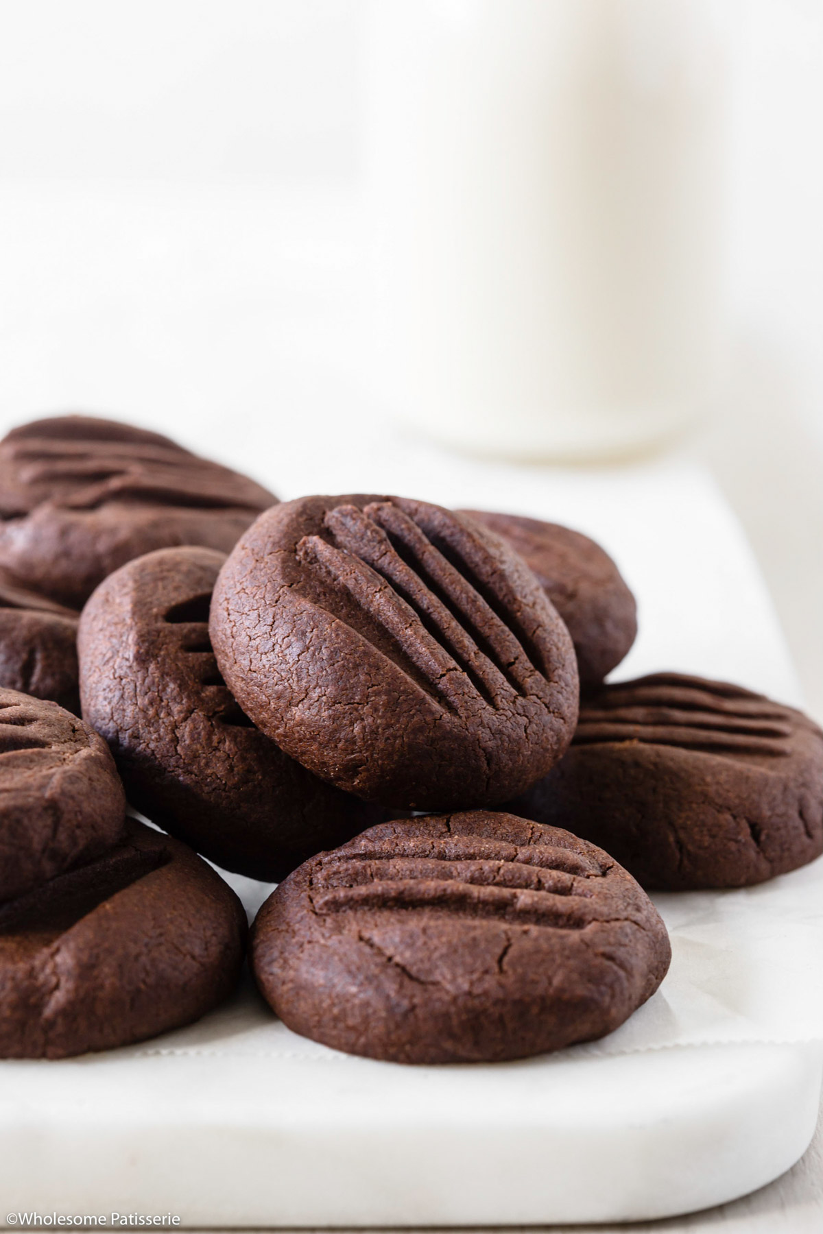Chocolate meltaway cookies stacked together in a pile on a white platter with a glass of milk behind.