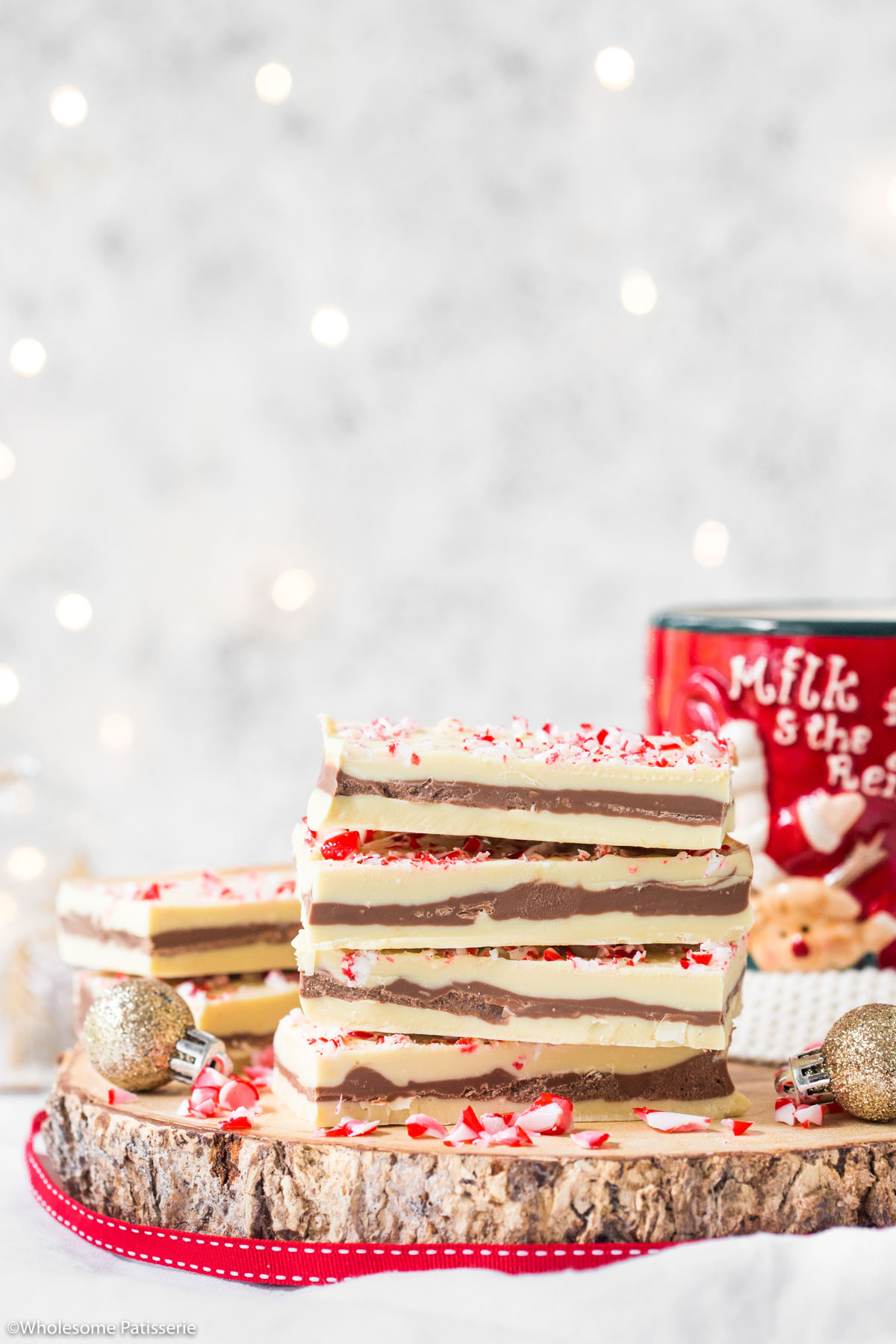 Peppermint chocolate candy cane bark on wooden platter with christmas mug and fairy lights behind 
