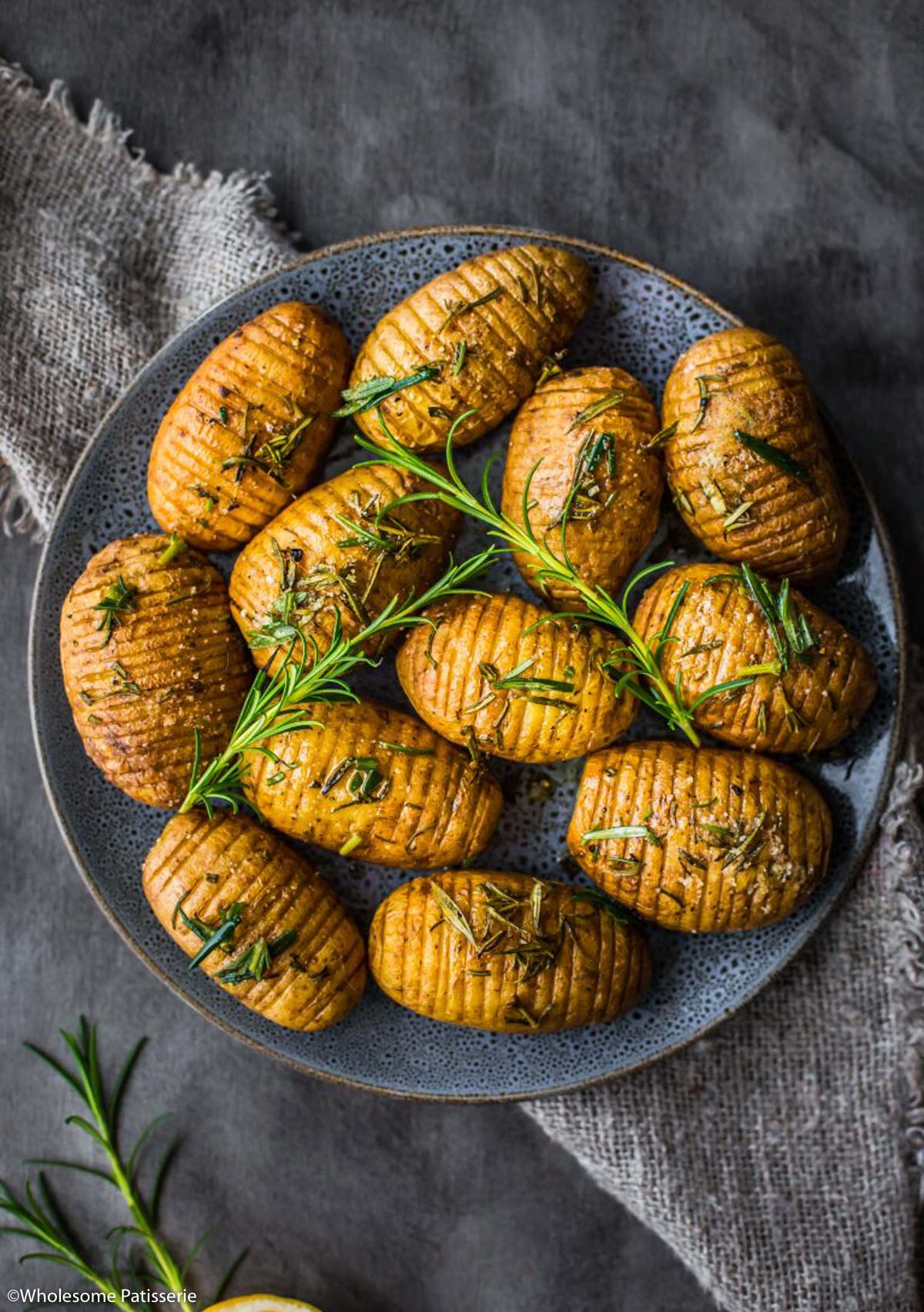 Hasselback potatoes on plate with fresh rosemary sprigs and a tea towel underneath. 