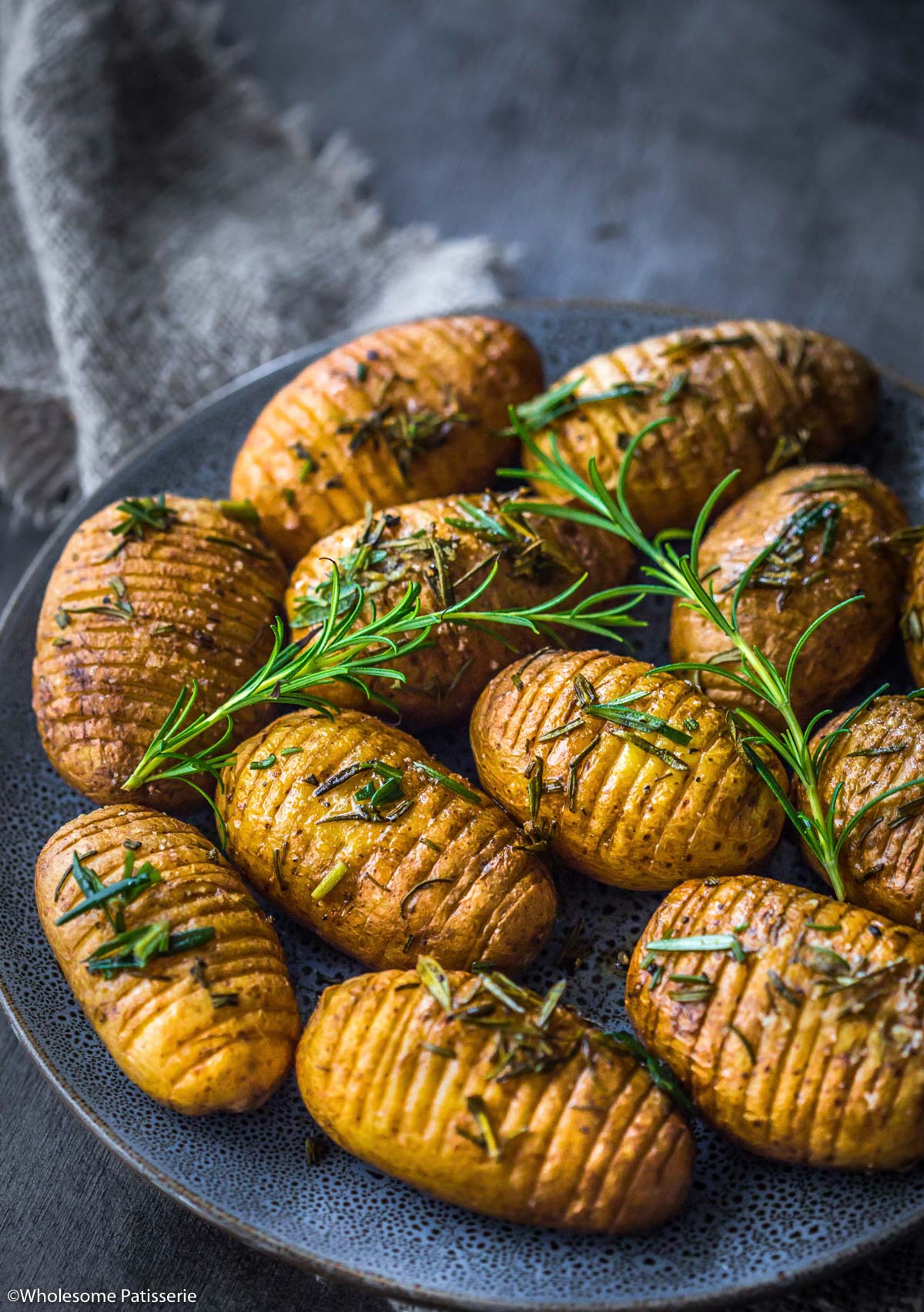 Air fried hasselback potatoes on plate garnished with fresh rosemary sprigs.