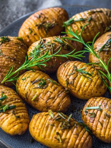 Air fried hasselback potatoes on plate garnished with fresh rosemary sprigs.
