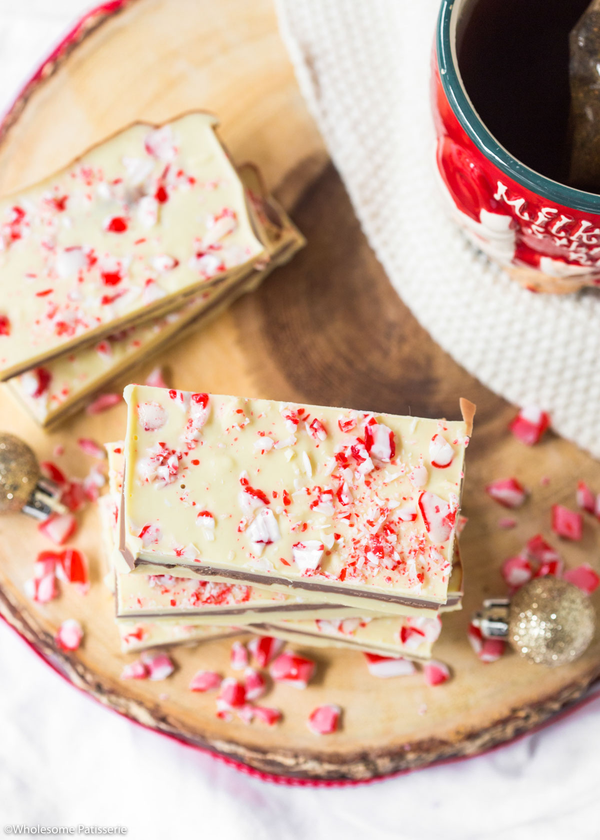 Candy cane bark on wooden platter with red ribbon and next to a christmas mug with candy cane pieces scattered.
