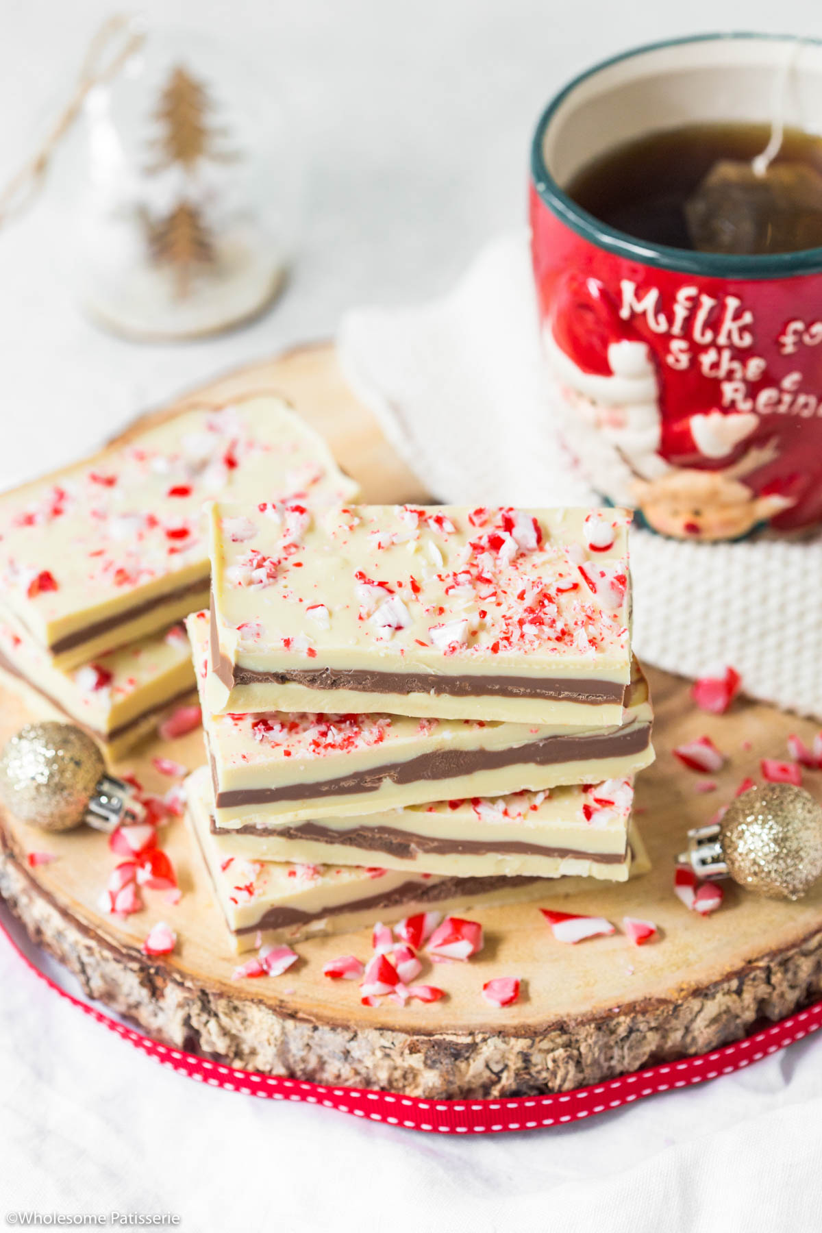Candy cane bark on wooden platter with red ribbon and next to a christmas mug.