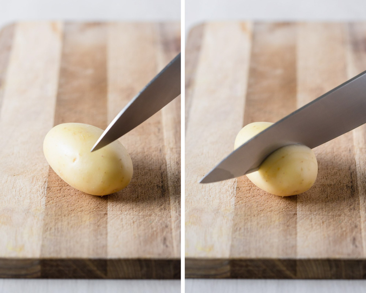Cutting one potato on wooden board with knife.
