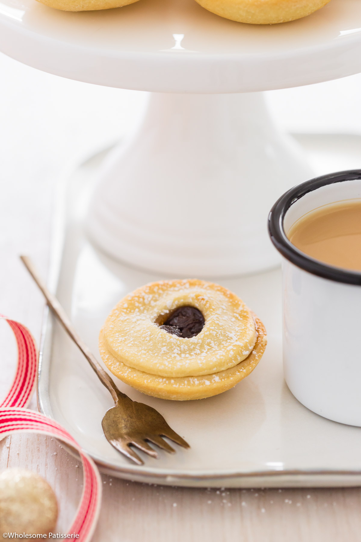 One mince pie on plate next to a cup of tea, a fork and christmas ribbon.