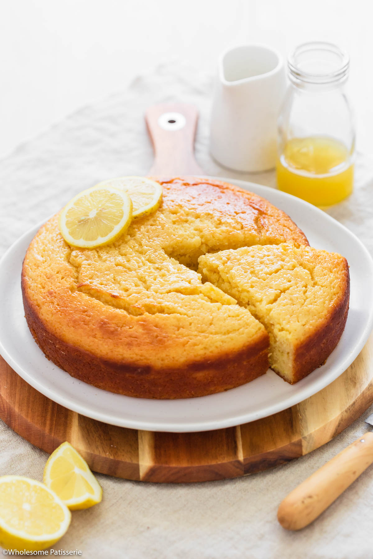 Easy lemon syrup cake decorated with fresh lemon slices on a round wooden board.
