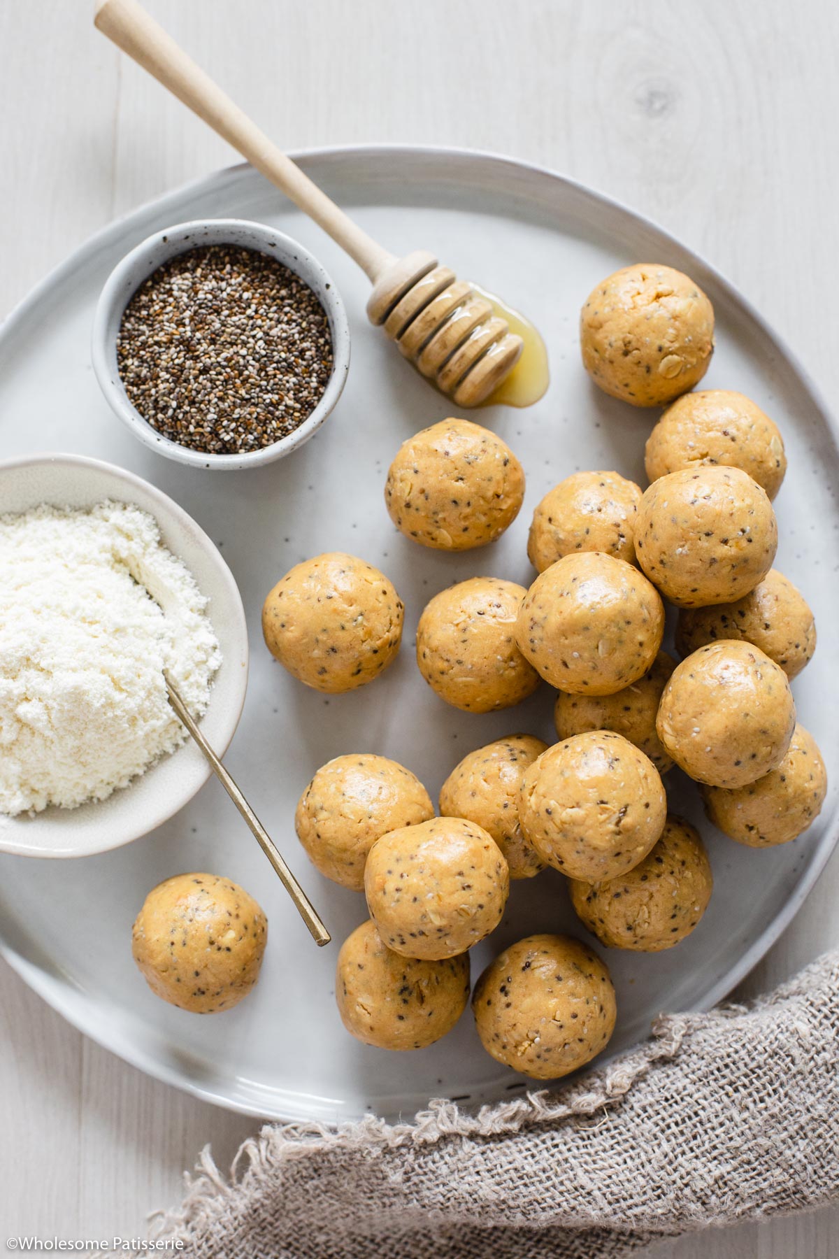 Peanut butter protein balls on plate next to a bowl of protein powder, chia seeds and honey.