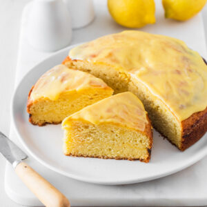 Simple lemon curd cake sliced and on a white plate with lemons behind