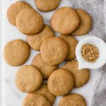 Homemade gingernut biscuits displayed on white marble board next to small bowl of ground ginger
