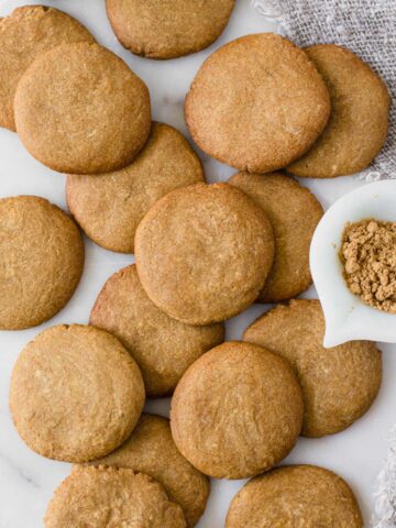 Homemade gingernut biscuits displayed on white marble board next to small bowl of ground ginger