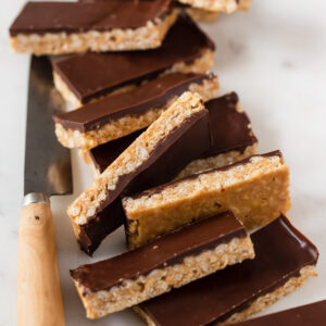 Chocolate peanut butter crunch bars stacked together on white board.