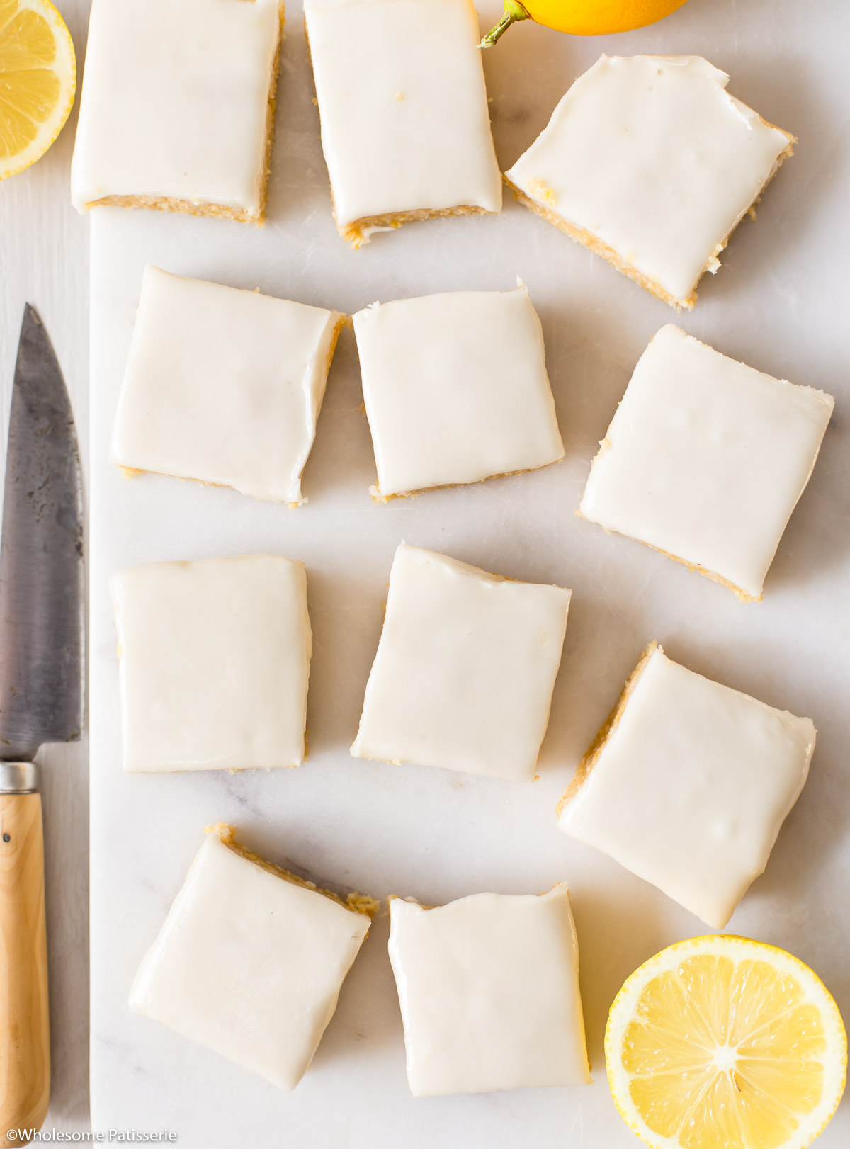 Slices of vegan lemon slice displayed on marble platter next to slices of fresh lemon and a decorative knife