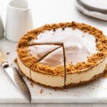 Cheesecake on board with crushed biscuits sprinkled on top and two slices cut out of it.