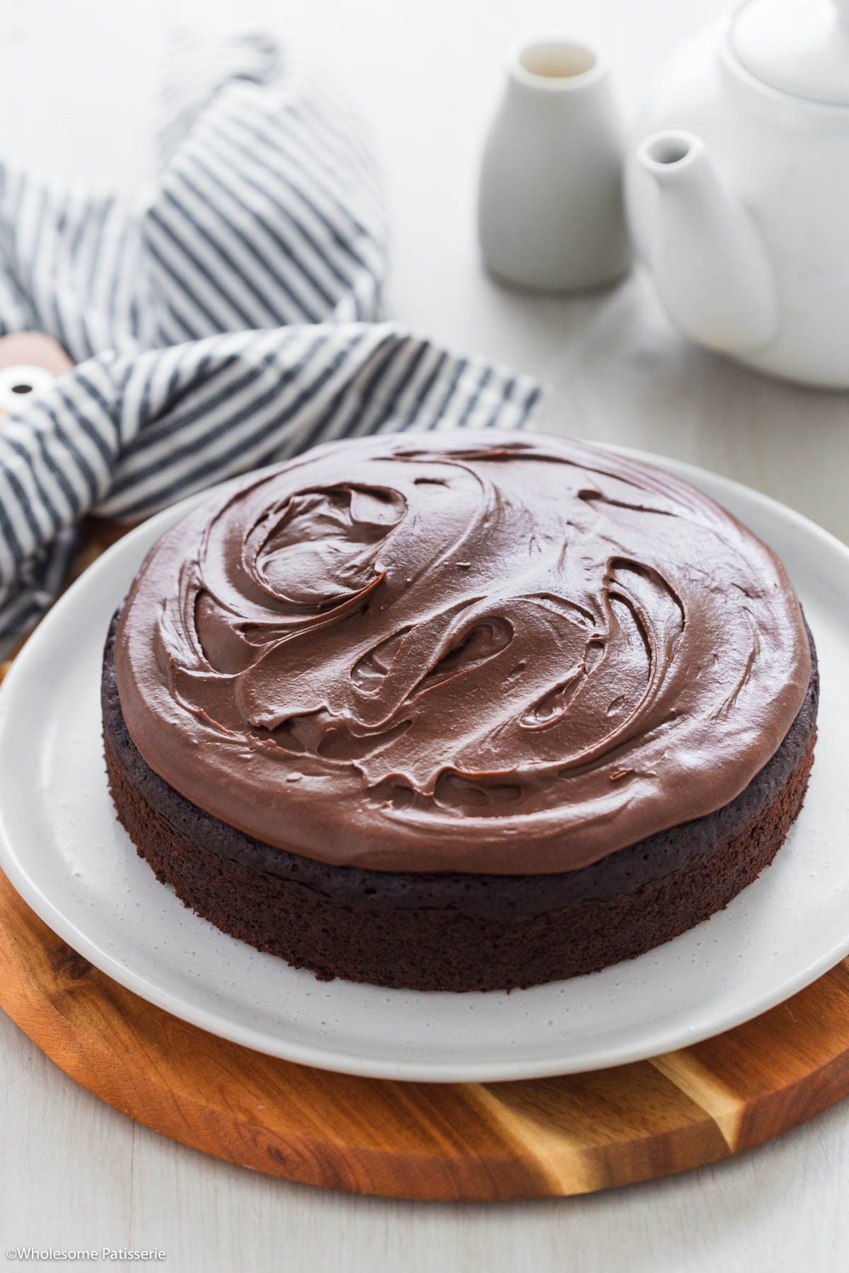 Chocolate fudge cake whole and frosted served on plate on top of wooden board