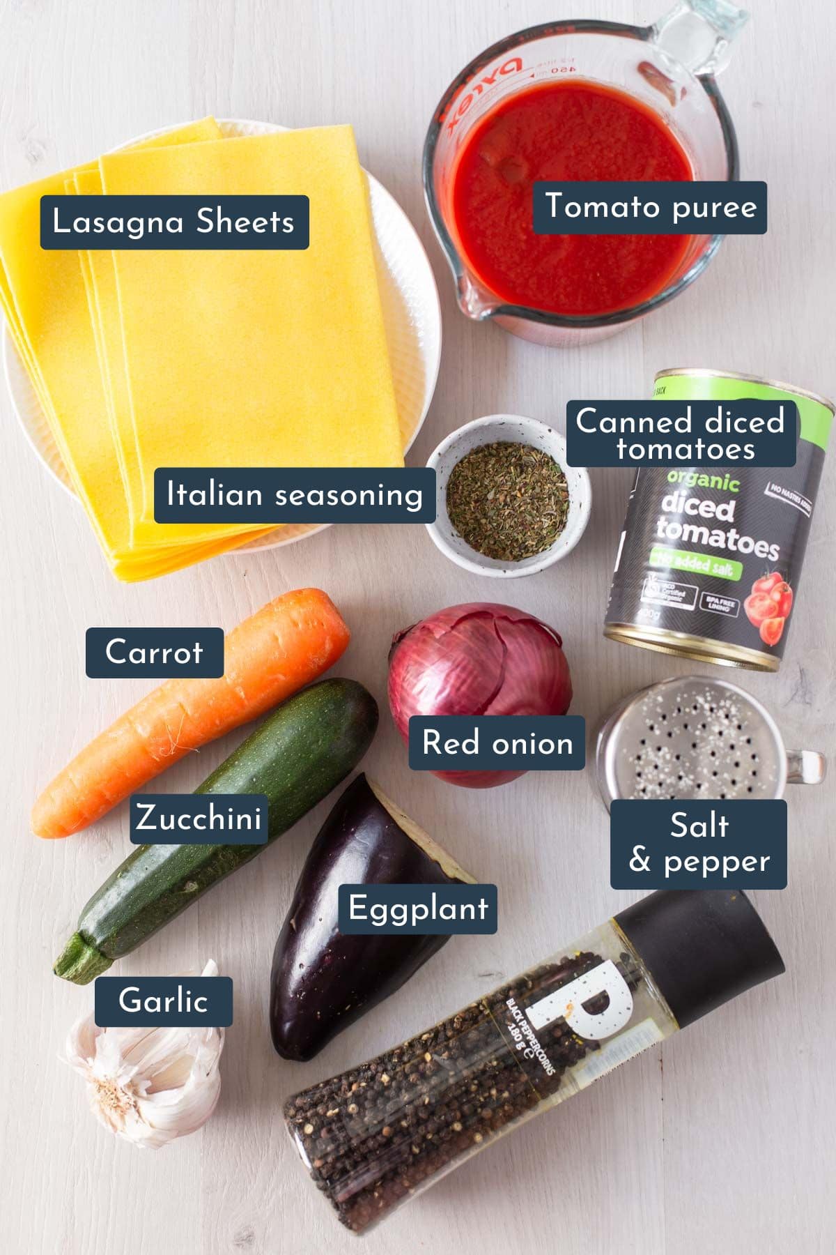Individual ingredients laid out to make vegetable tomato mixture is lasagna sheets, tomato puree, canned diced tomatoes, dried Italian seasoning, red onion, carrot, zucchini, eggplant, garlic, salt and pepper.