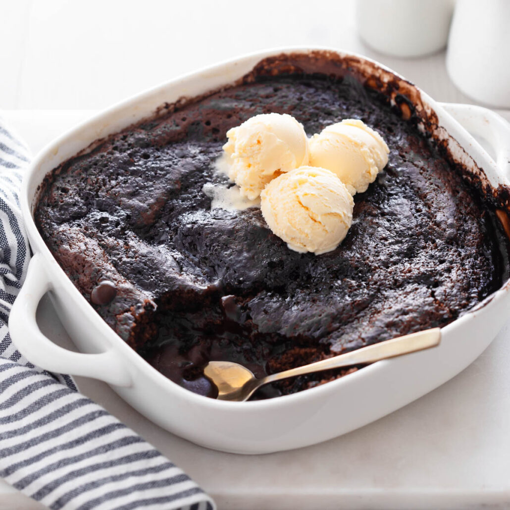 Chocolate self saucing pudding in baking dish with gold spoon and scoops of vanilla ice cream