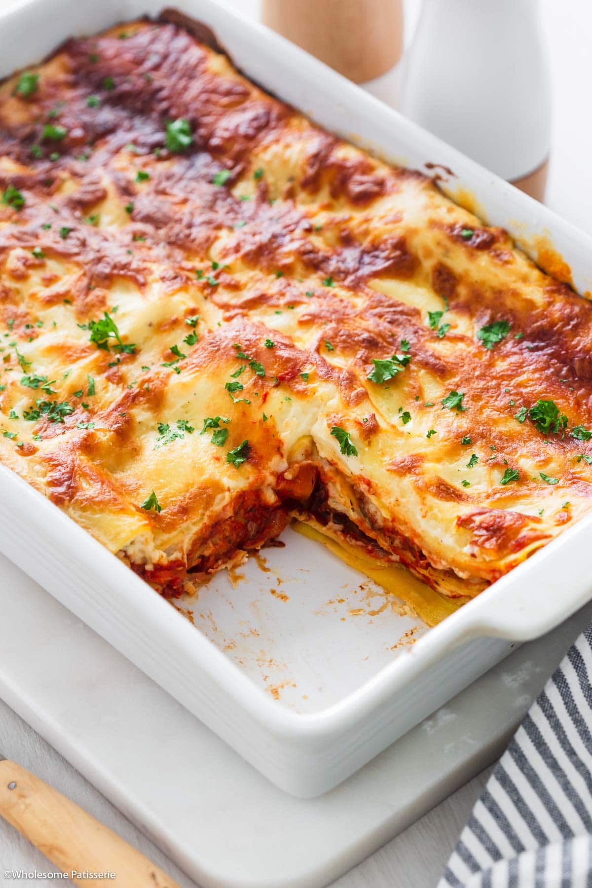 Lasagna in white baking dish sprinkled with fresh parsley and with one slice removed.