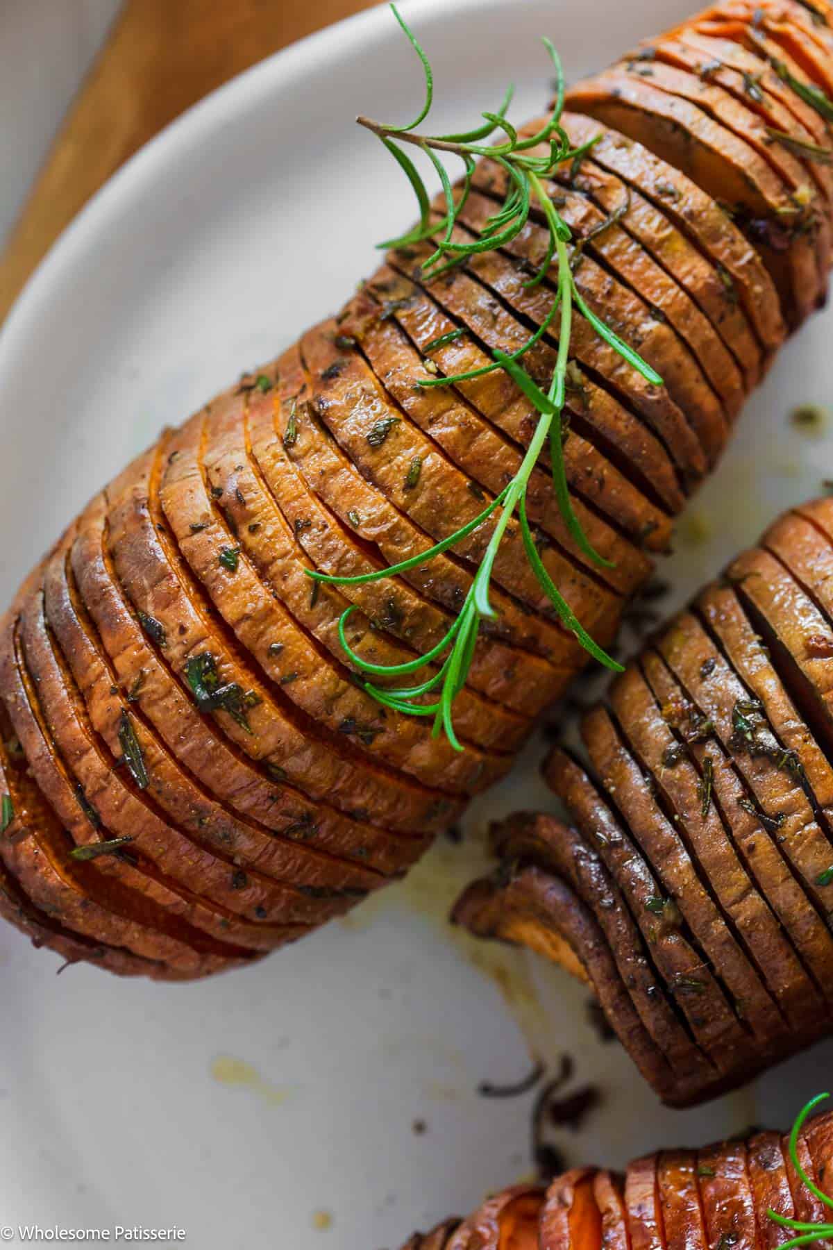 Overhead close up view of one hasselback sweet potato with fresh rosemary on top.