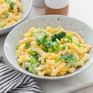 Pasta with broccoli in bowl garnished with sliced green onions.