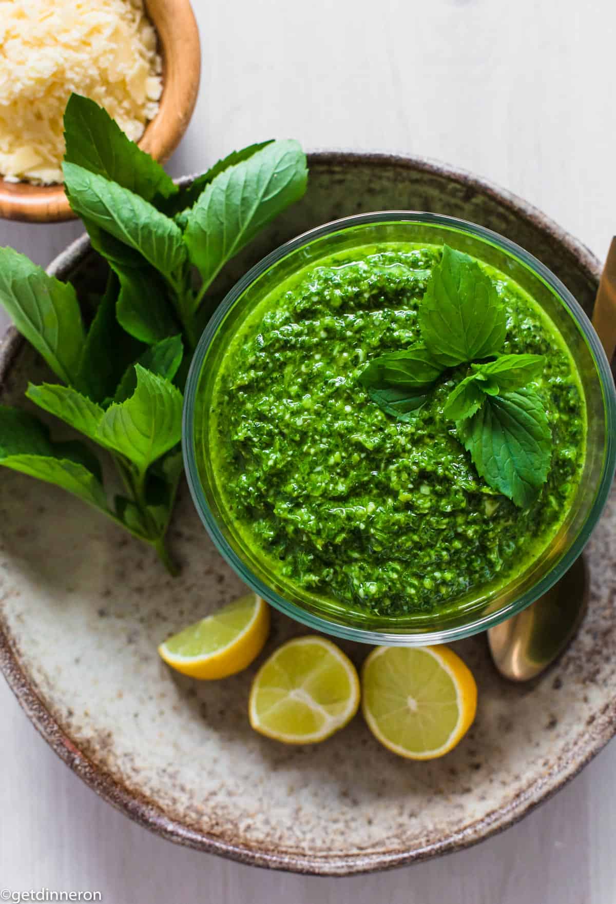 Overhead view of pesto in glass bowl surrounded by fresh cut lemons and basil leaves.