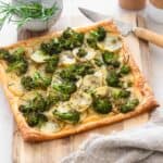 Cooked tart on wooden chopping board with bowl of fresh rosemary herbs behind.
