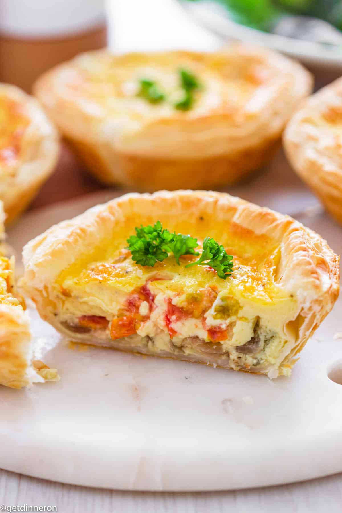One quiche sliced in half to show filling while sitting on marble white platter.