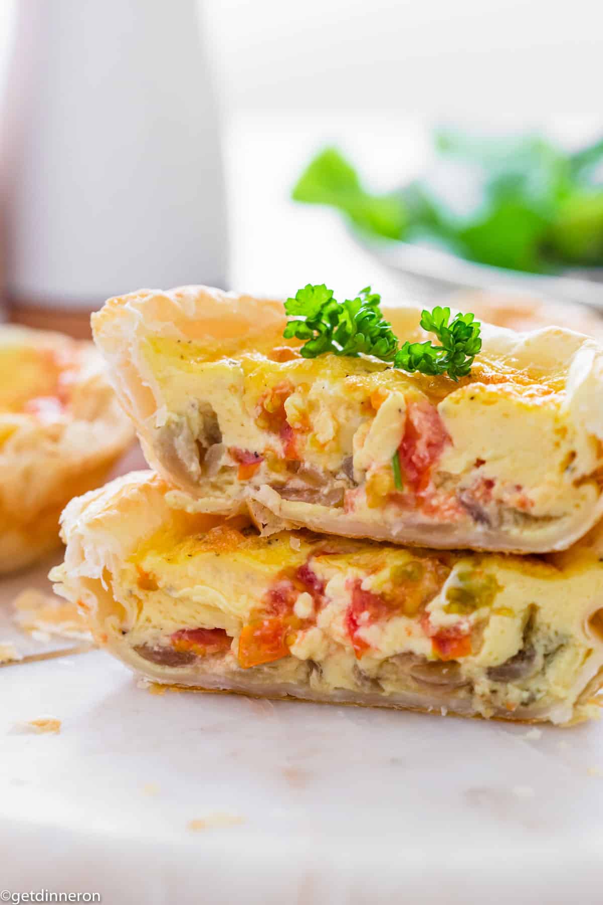 One puff pastry quiche cut in half with both stacked on top of each other and garnised with fresh parsley.