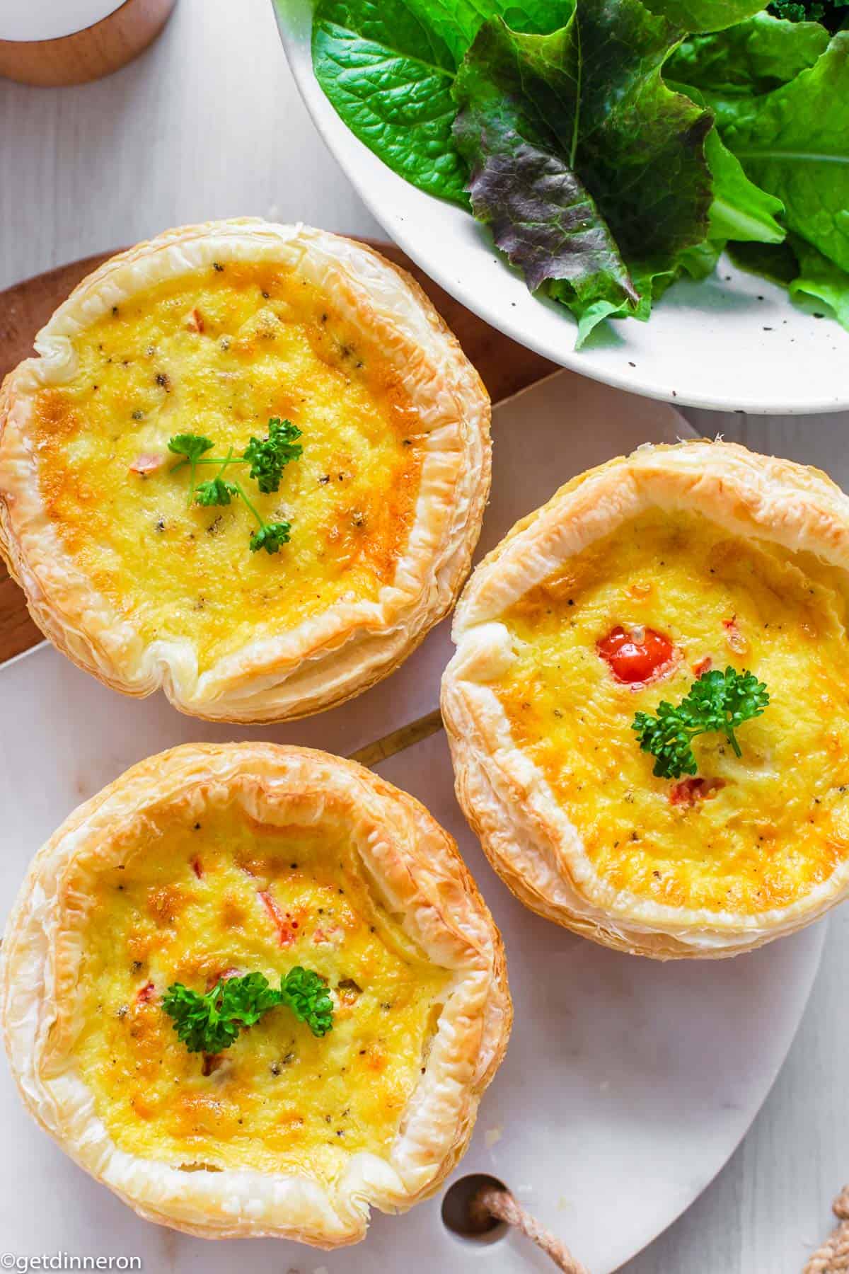 Overhead view of quiches garnished with fresh parsley and sitting on marble platter.