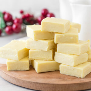 White chocolate fudge cut into squares stacked together on wooden board.