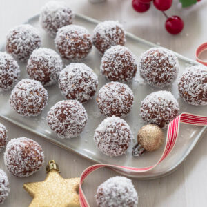Traditional rum balls recipe on serving platter with Christmas decorations surrounding.