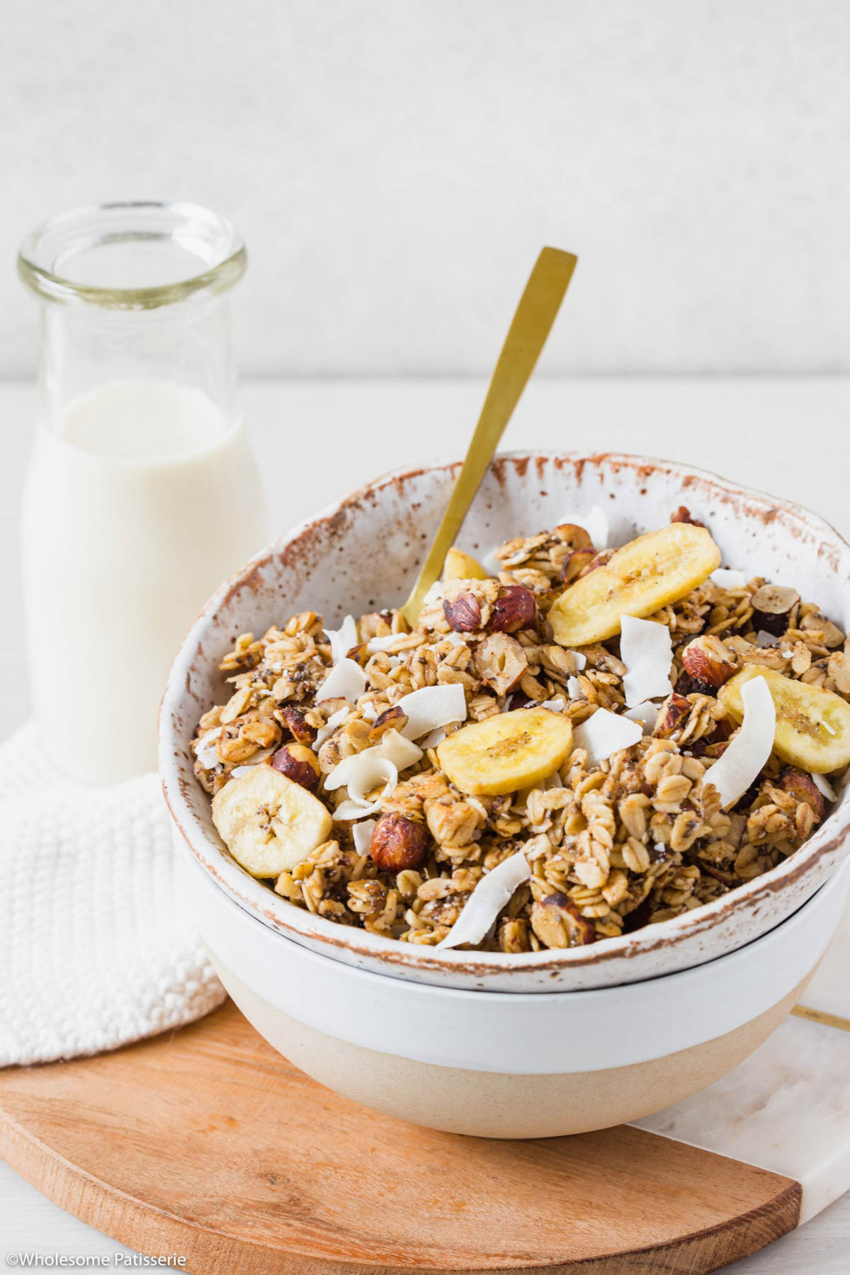 Banana bread granola in bowl with spoon and glass of milk behind.