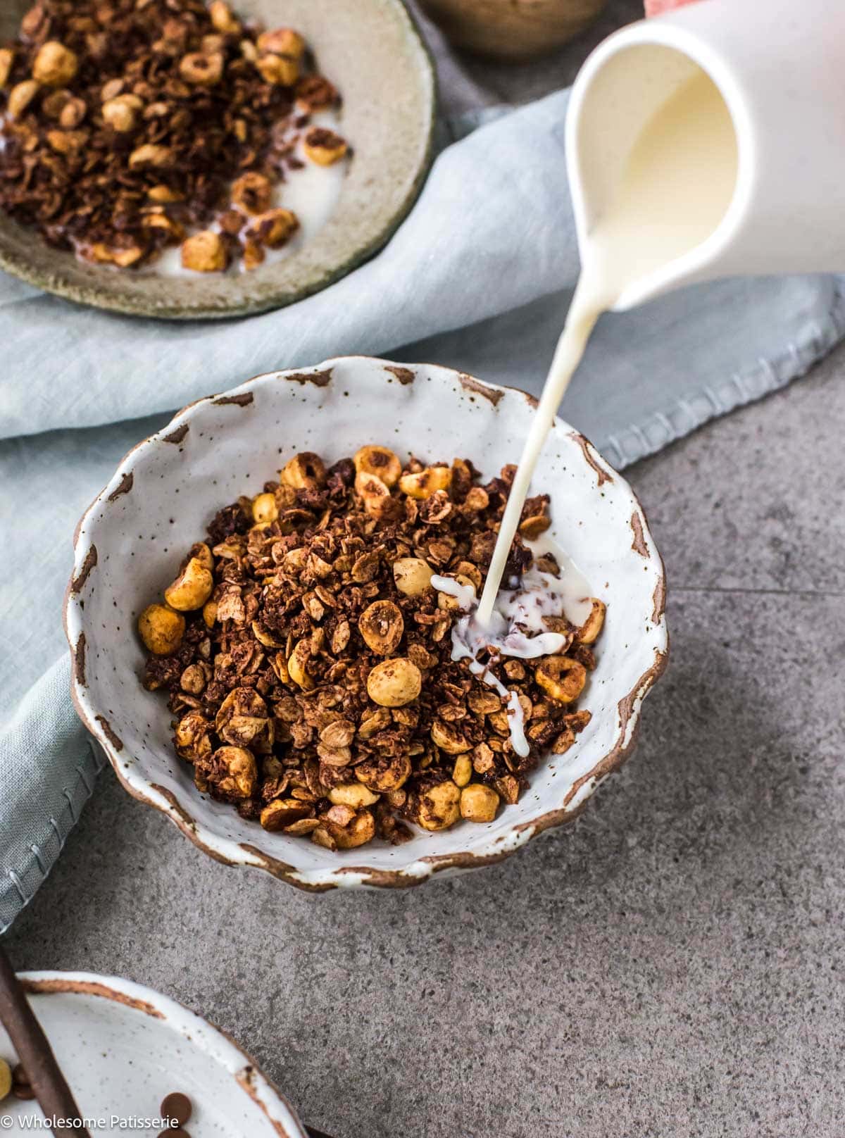 Hazelnut granola in cereal bowl with milk being poured in.
