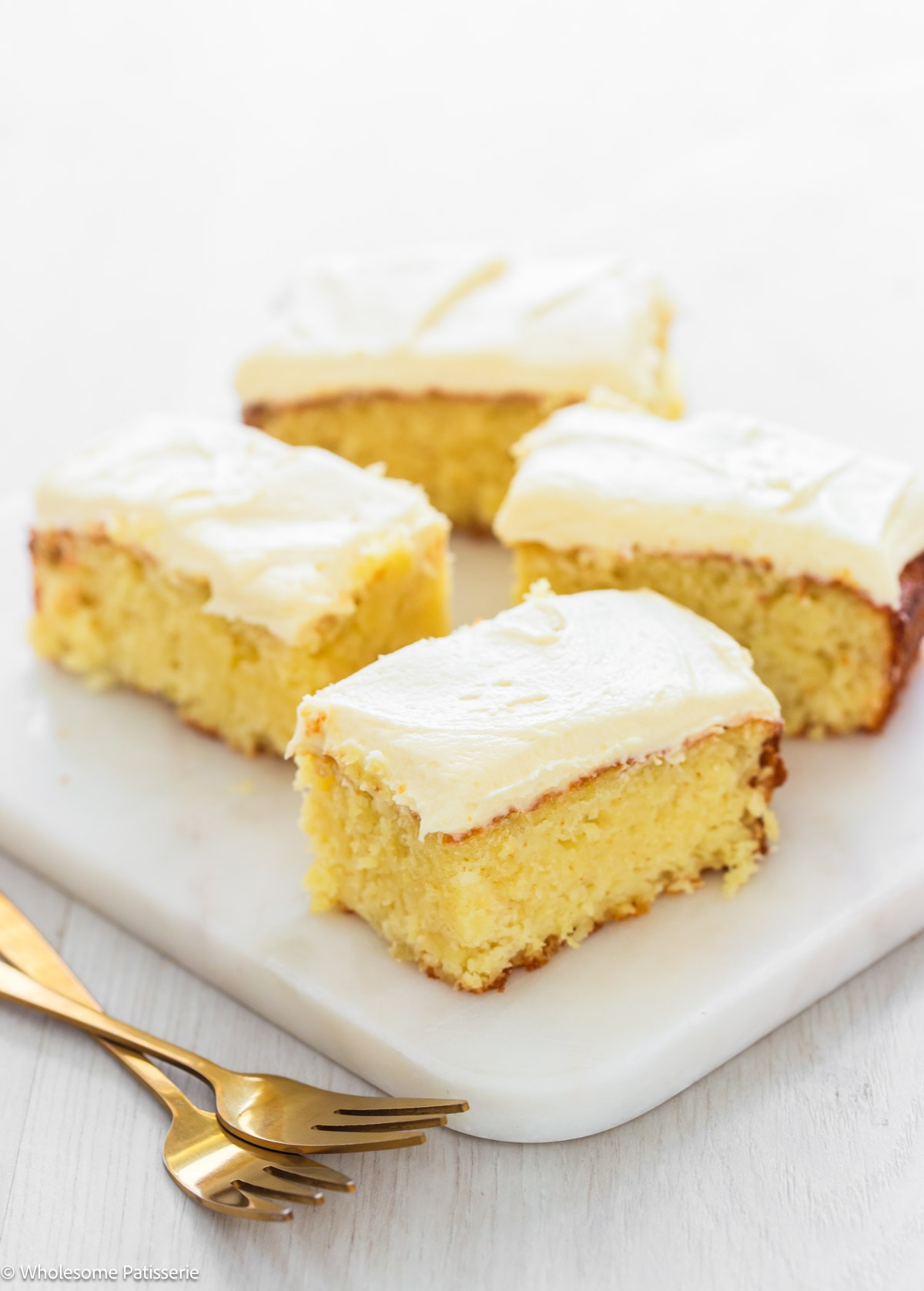 Cake mix pineapple cake slices with cream cheese frosting sitting on white platter.