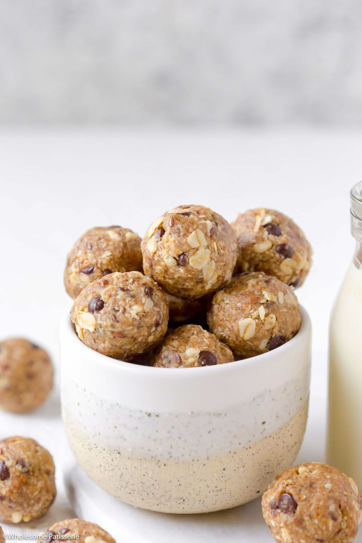 Granola snack balls stacked together in bowl next to glass of milk.