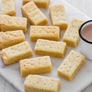 Shortbread biscuits displayed on marble board next to cup of tea.