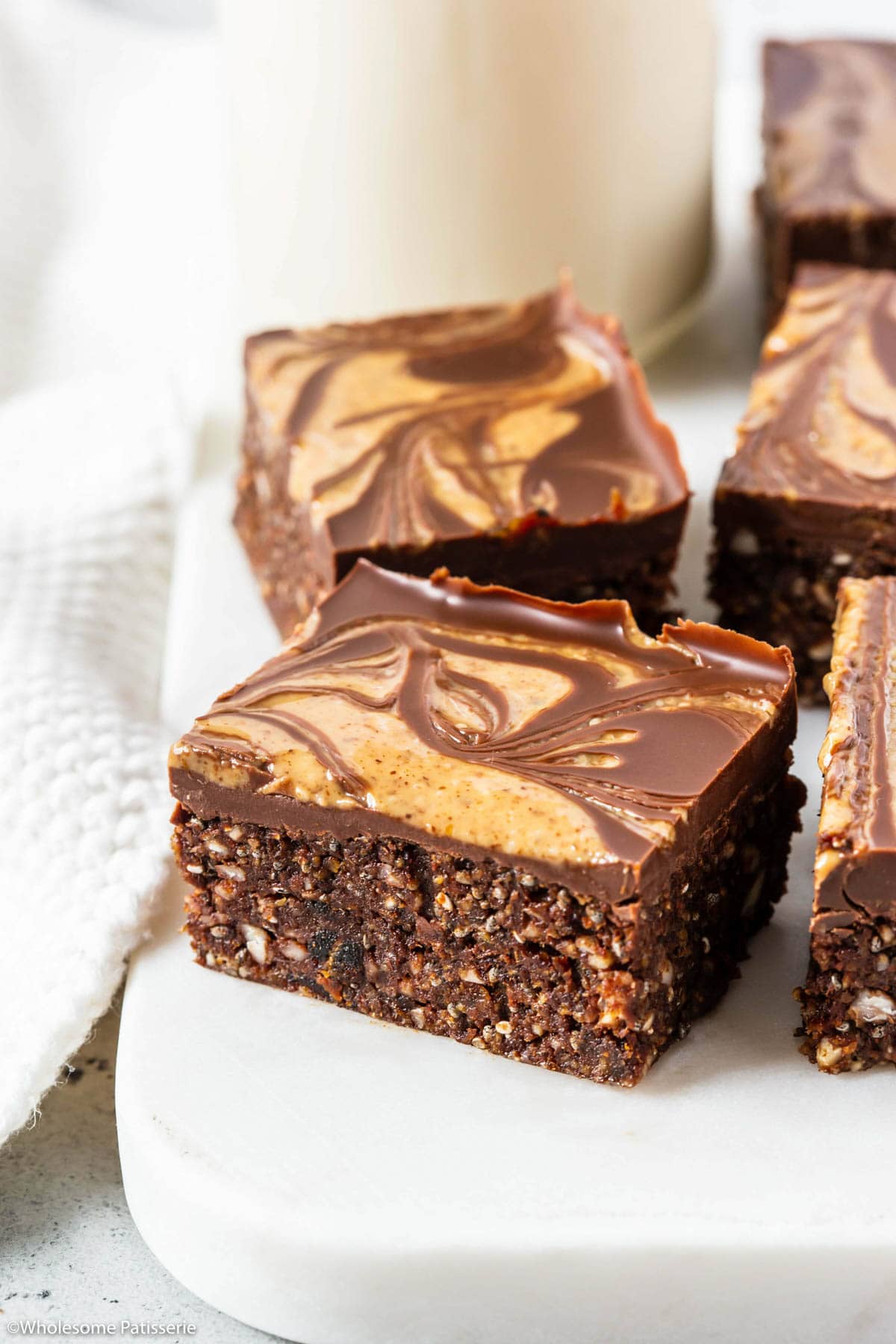 One sliced square of no bake brownies with chia seeds sitting on white board next to more cut brownies.