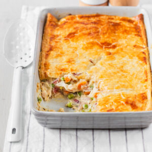 Chicken pot with with puff pastry in baking dish with one serve taken out.