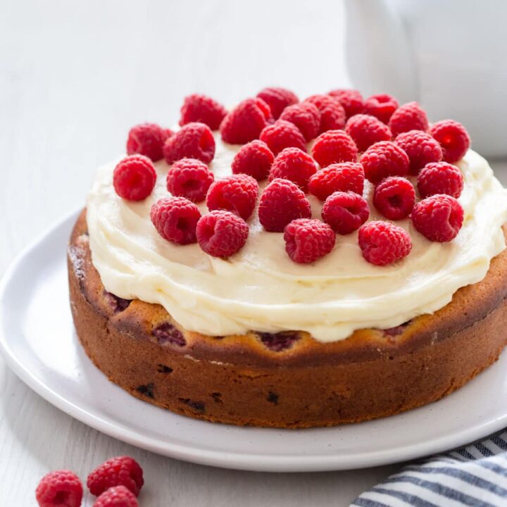 Summer raspberry cake on plate garnished with fresh raspberries.