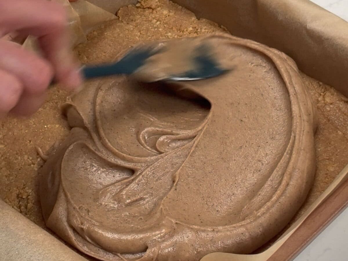 Spreading pumpkin spice icing on top of biscuit base in pan.