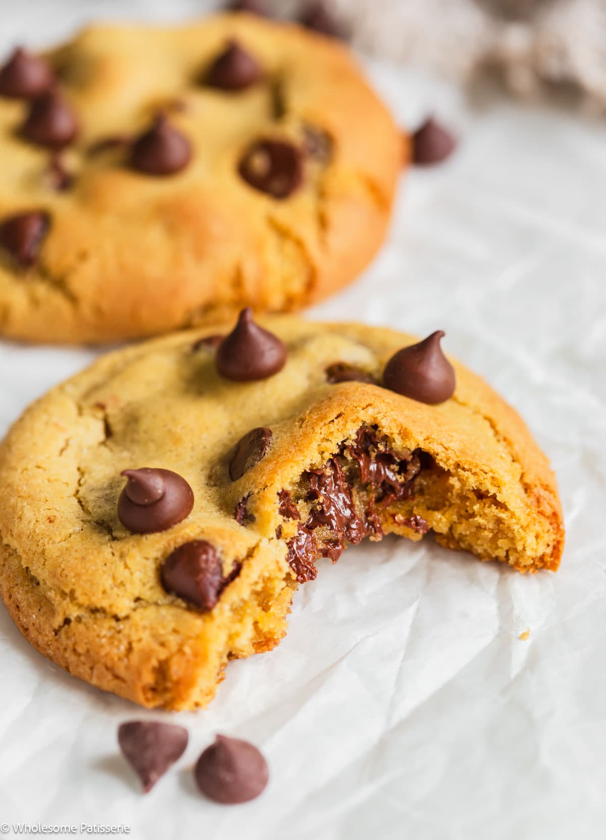 Chocolate chip cookie with bite taken out and sitting on white parchment paper.