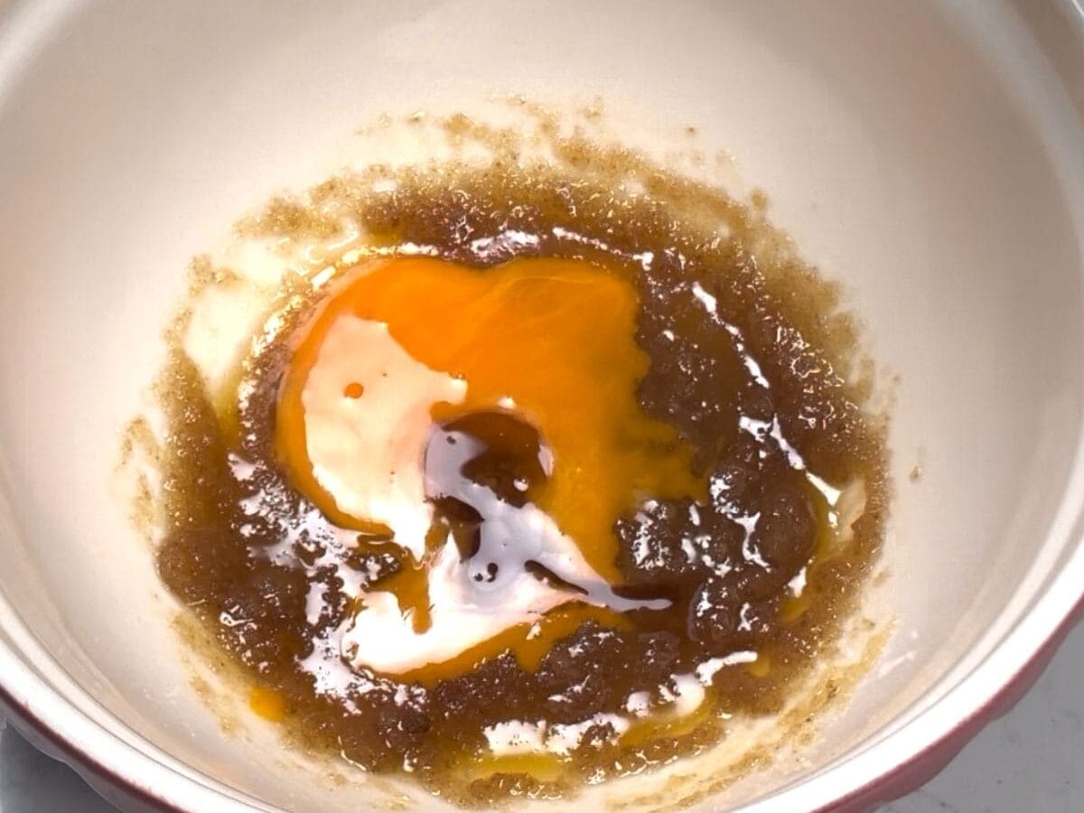 Whisking egg yolk and vanilla into melted butter and sugar.