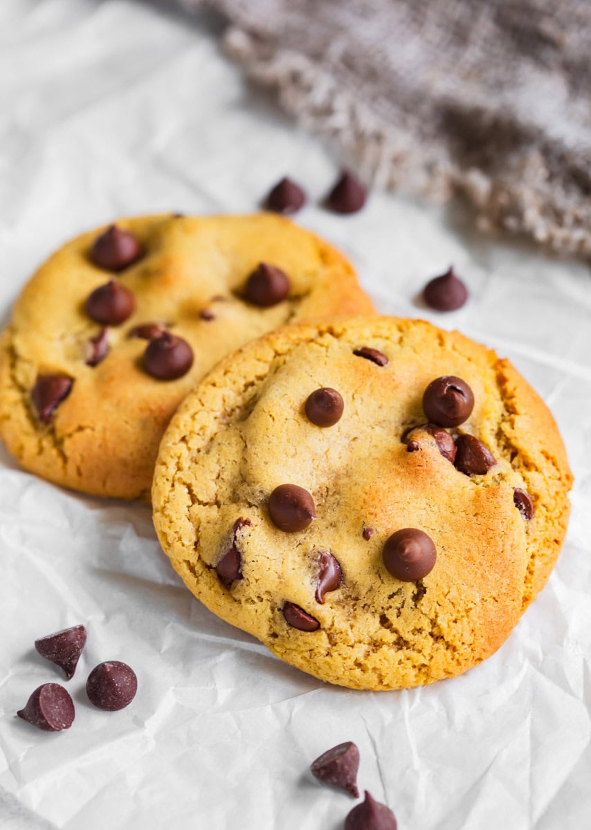 Two chocolate chip cookies with chocolate chips surrounding.