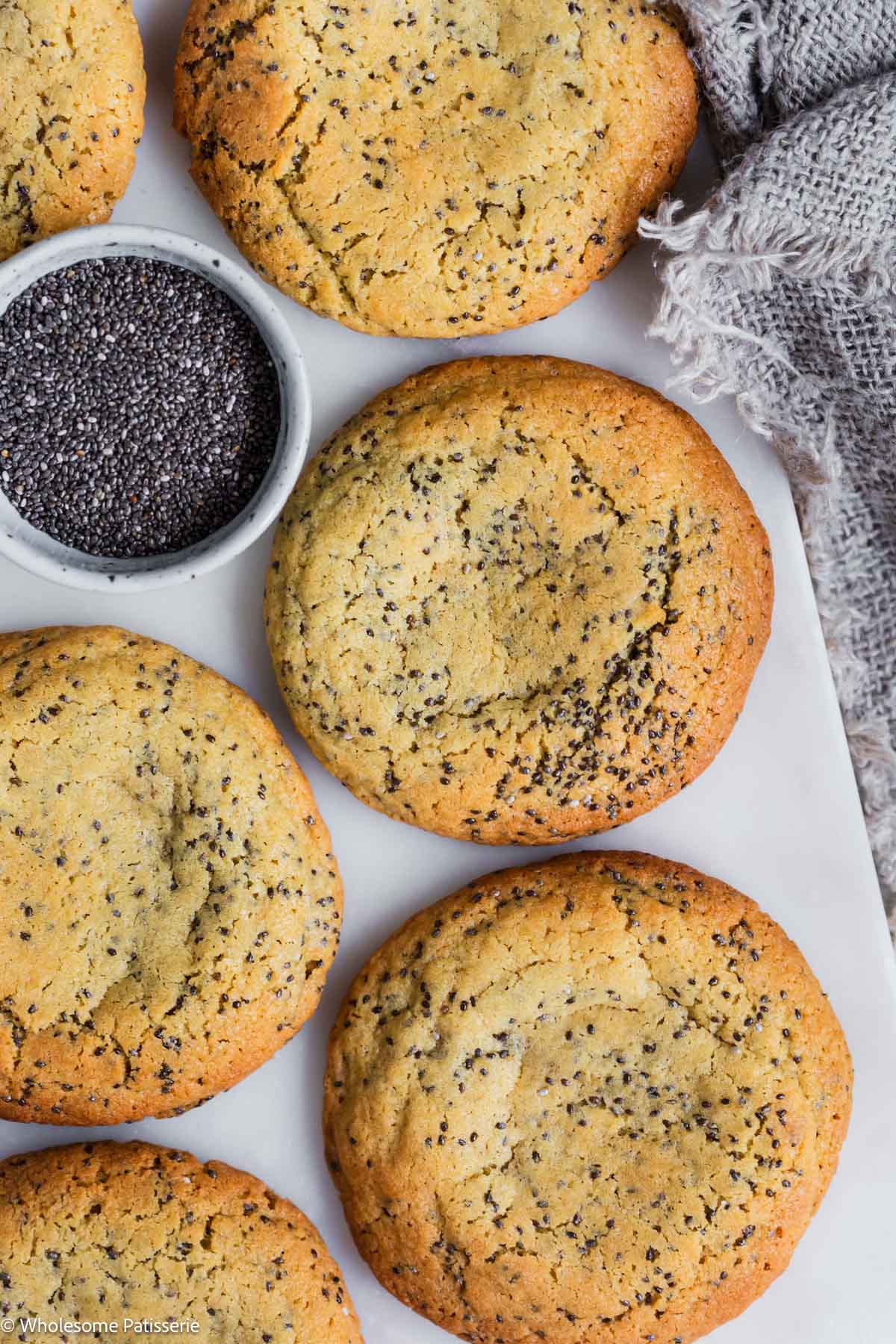 Big soft chia seed cookies on marble board with small bowl of chia seeds.
