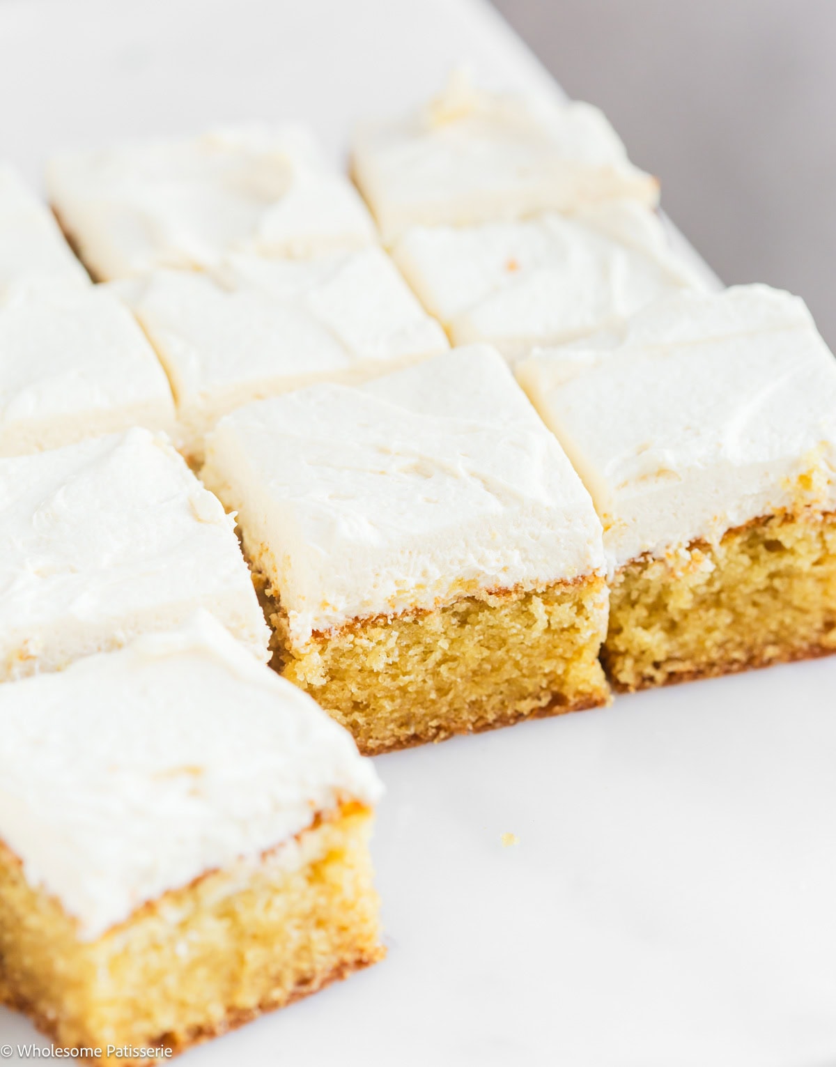 Vanilla cake without milk and eggs cut into squares on marble board with vanilla frosting.