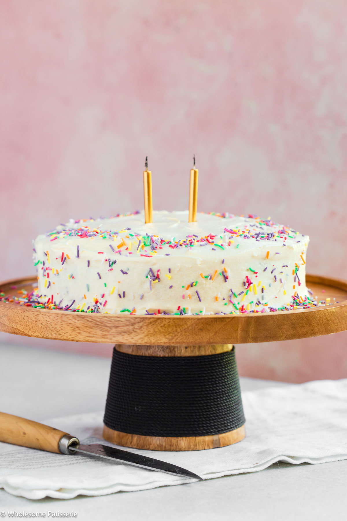 One layer birthday cake on cake stand with candles and sprinkles surrounding.