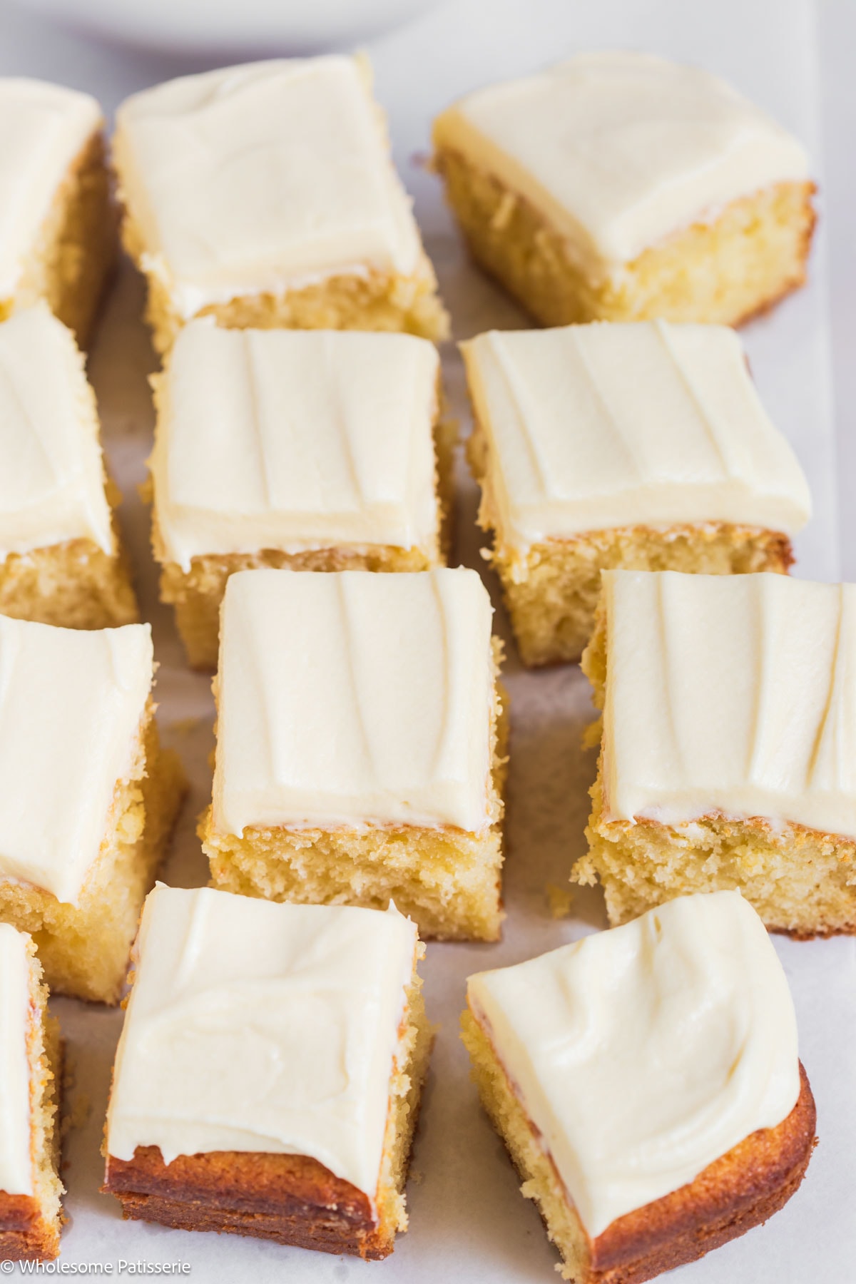 Vanilla cake without vanilla extract cut into squares displayed on board.