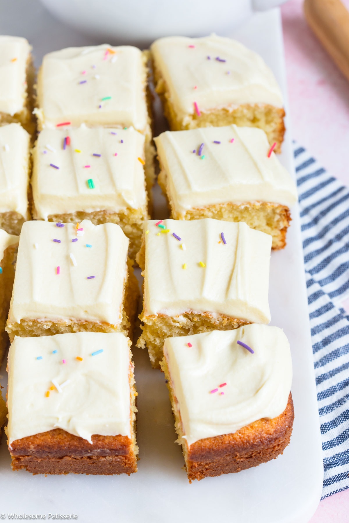 Vanilla cake without cake flour cut into squares and displayed on board with frosting and sprinkles.